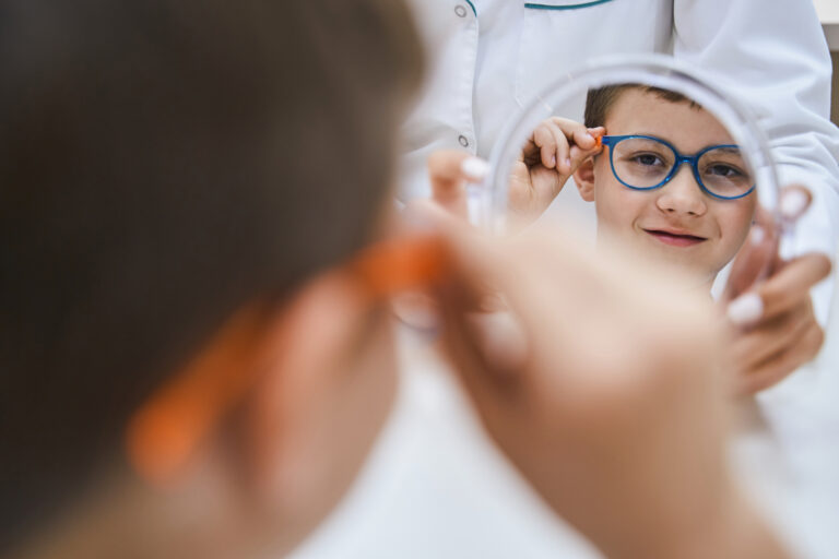 Cute male child trying on eyeglasses and smiling while having appointment with doctor optometrist